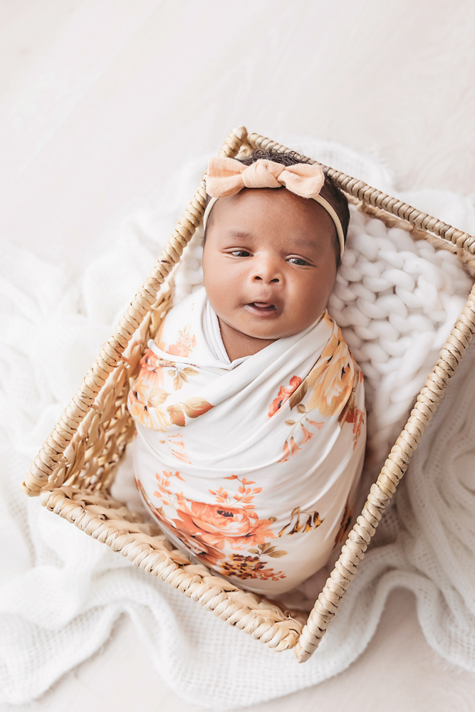 Newborn Lily wrapped in floral swaddle inside a wicker basket with peach bow at Reflection Images by Tracy Rowell in Florence SC