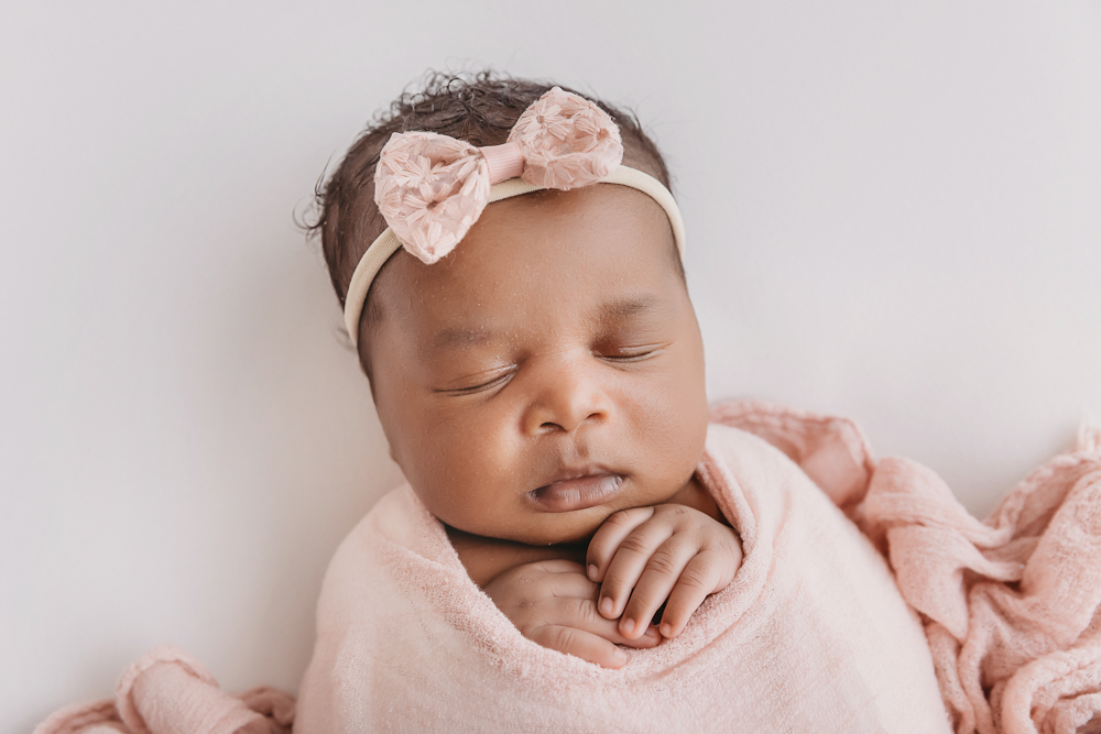 African American newborn Lily sleeping portrait with textured bow headband against clean white backdrop at Reflection Images by Tracy Rowell in Florence SC