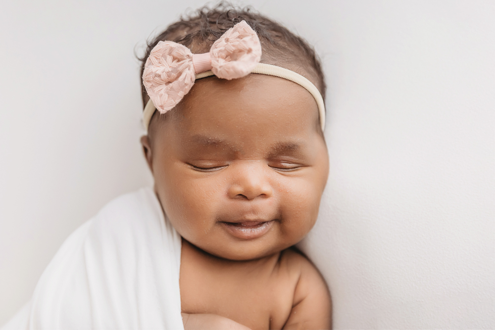 Newborn Lily smiling close up wearing a pink bow with creamy backdrop at Reflection Images by Tracy Rowell in Florence SC