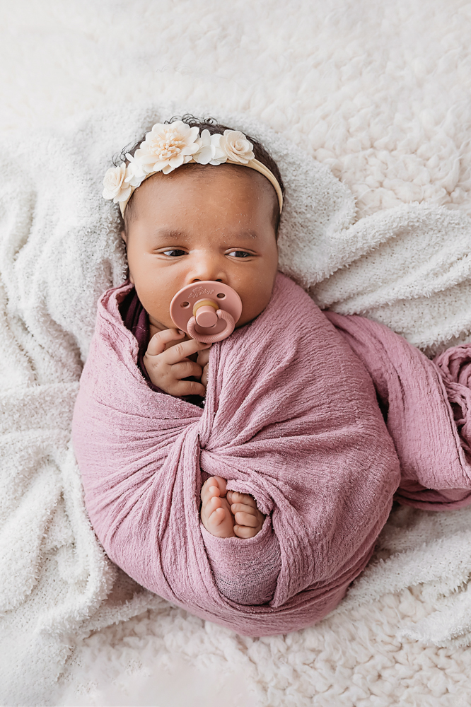African American newborn Lily snuggled in mauve wrap with pacifier on textured blanket at Reflection Images by Tracy Rowell in Florence SC