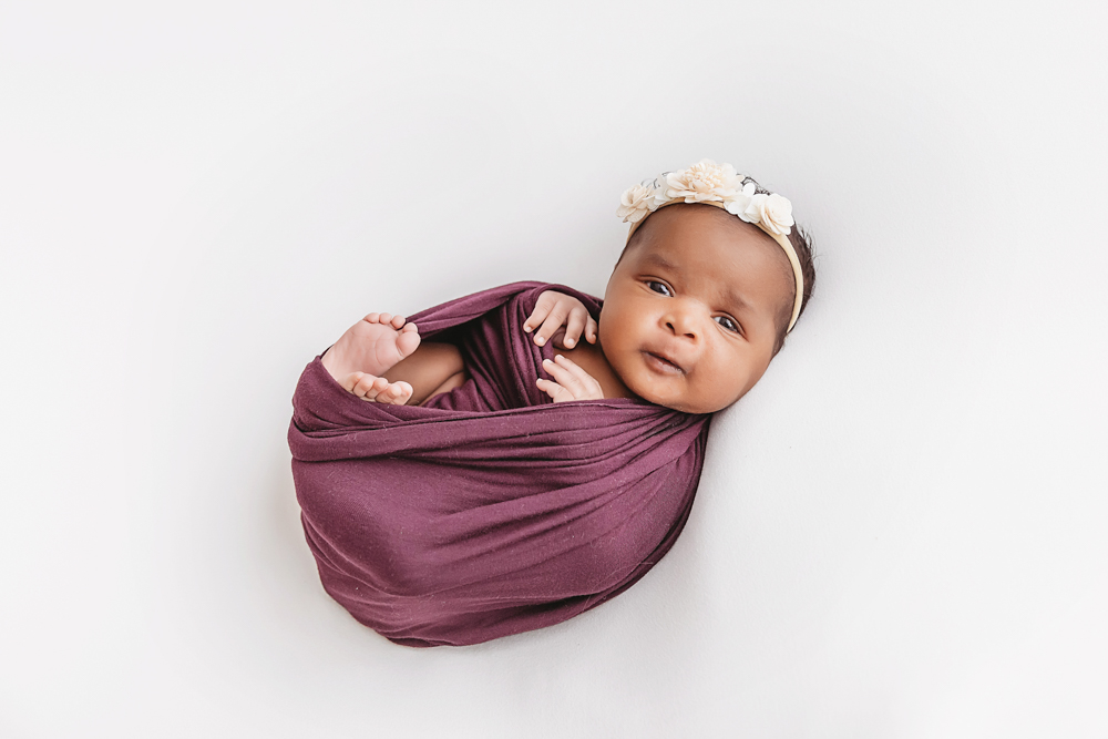 Newborn Lily angled view in plum wrap with tiny feet poking free at Reflection Images by Tracy Rowell in Florence SC
