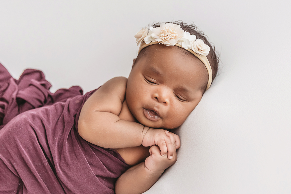 Newborn Lily side lying pose in deep plum wrap with floral headband at Reflection Images by Tracy Rowell in Florence SC