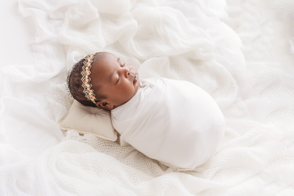 Newborn Lily sleeping on a tiny pillow in a white wrap and lace headband at Reflection Images by Tracy Rowell in Florence SC
