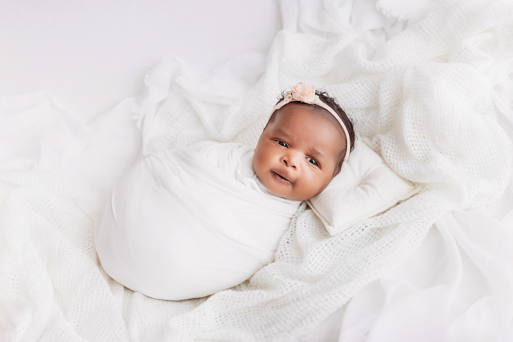 Newborn Lily wrapped in white with a soft peach flower headband on a cozy blanket at Reflection Images by Tracy Rowell in Florence SC