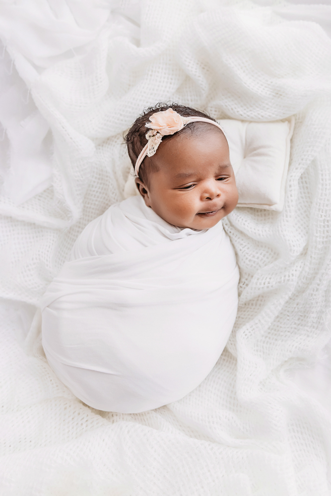 Newborn nestled in white, peach flower headband showing a gentle side profile at Reflection Images by Tracy Rowell in Florence SC