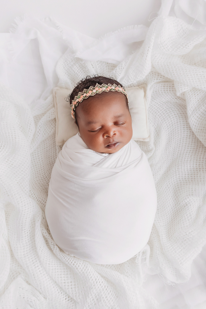 Newborn Lily top down view in a white swaddle with a petite peach headband at Reflection Images by Tracy Rowell in Florence SC