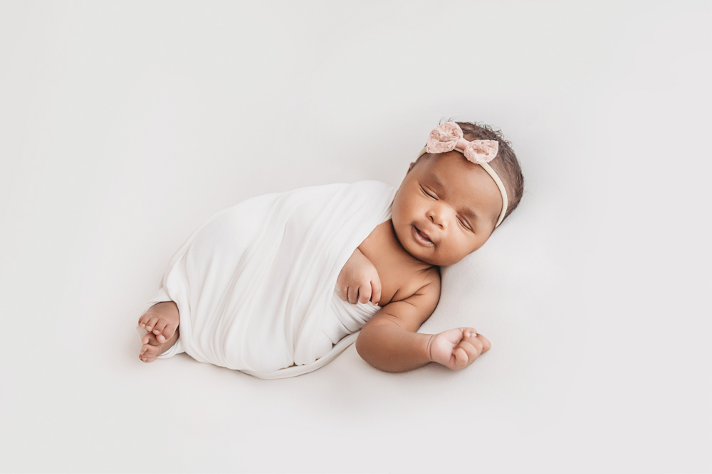 Newborn Lily white wrapped portrait with a sweet smile and relaxed pose at Reflection Images by Tracy Rowell in Florence SC