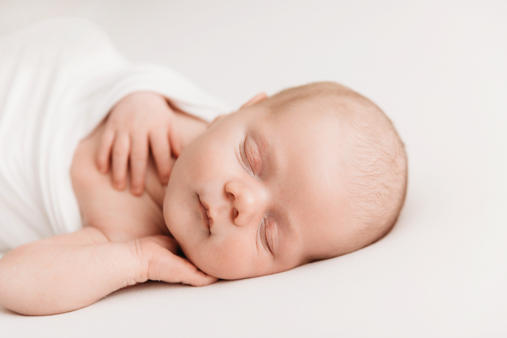 Beau sleeping on tummy wrapped in white with hands tucked under cheek on soft white backdrop at Reflection Images by Tracy Rowell in Florence SC