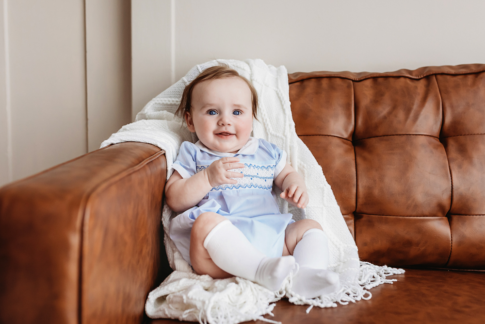 Baby boy in pale blue smocked romper lying on white blanket, professional photography studio Florence SC