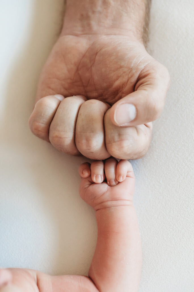 Newborn fist cradled in a parent's gentle hand on soft white blanket at Reflection Images by Tracy Rowell in Florence SC