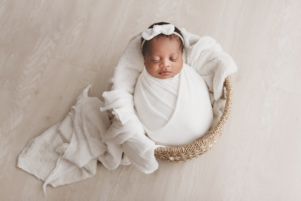 Harlem asleep in a woven basket, wrapped in white with a bow headband on soft neutral layers at Reflection Images by Tracy Rowell in Florence SC