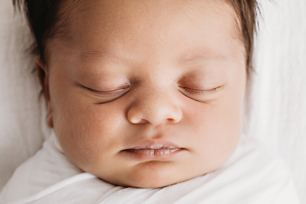 Close-up of newborn Liston's face with amazing hair, swaddled in white and resting on a white blanket at Reflection Images by Tracy Rowell in Florence SC