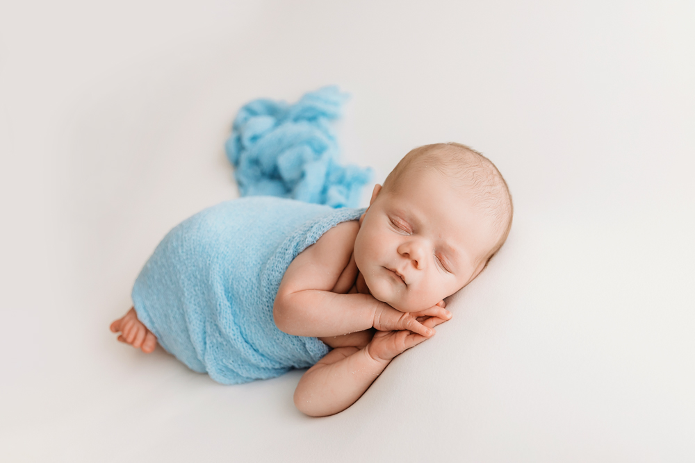 Beau in a blue wrap lying on his side with hands under chin on bright white background at Reflection Images by Tracy Rowell in Florence SC