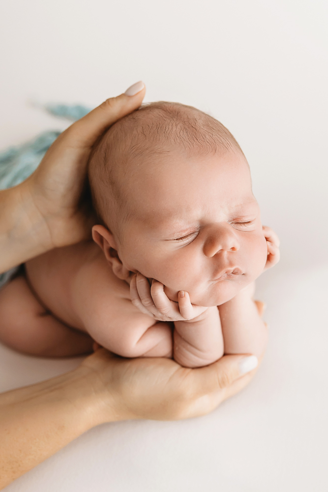 Froggy pose of Beau with his face resting in his hands supported by adult hands on white backdrop at Reflection Images by Tracy Rowell in Florence SC