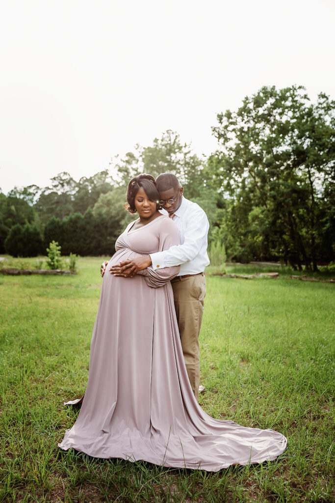 Partner embraces from behind with hands on her belly, soft evening light in Florence SC.