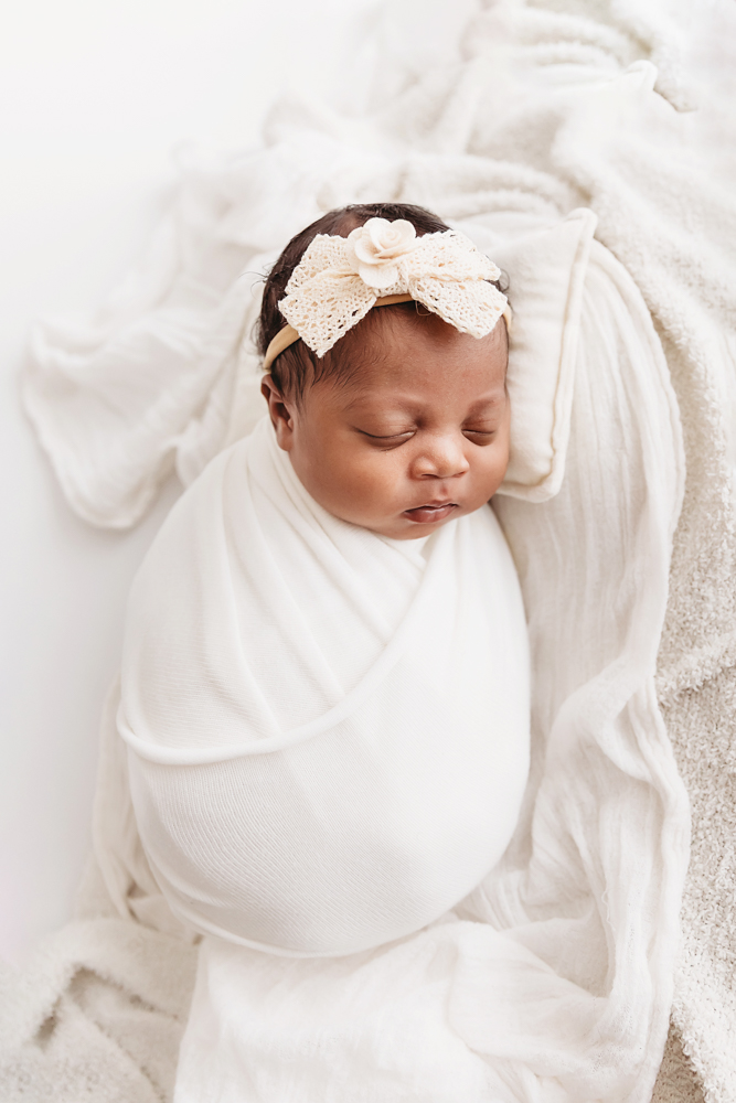 Harlem resting on soft white layers, swaddled in a white wrap with a lace cream bow headband at Reflection Images by Tracy Rowell in Florence SC