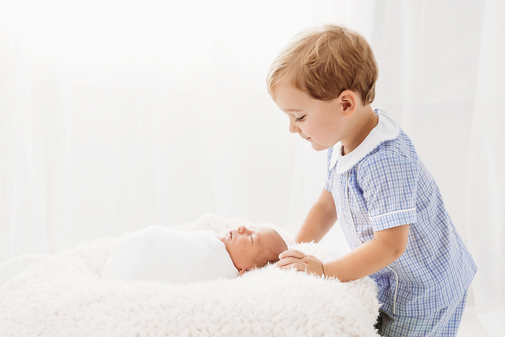 Tommy gently placing a hand on newborn Harry wrapped in white on cream flokati at Reflection Images by Tracy Rowell in Florence SC