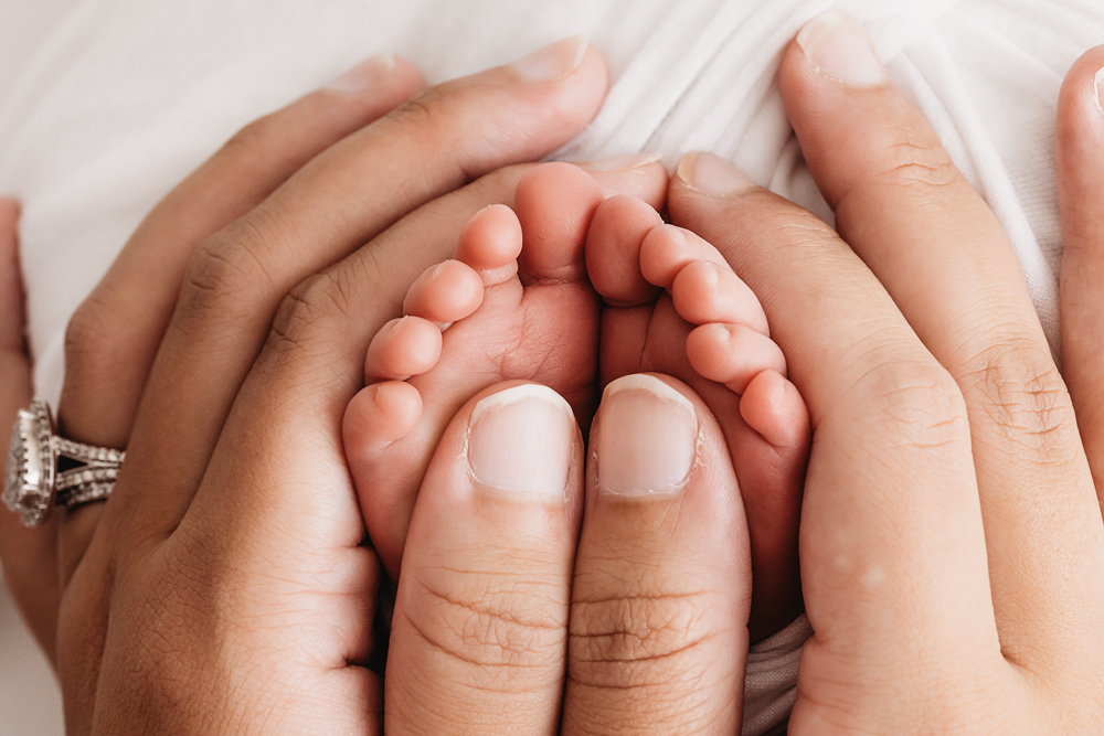 Macro shot of newborn Liston's tiny feet held gently by parents hands at Reflection Images by Tracy Rowell in Florence SC