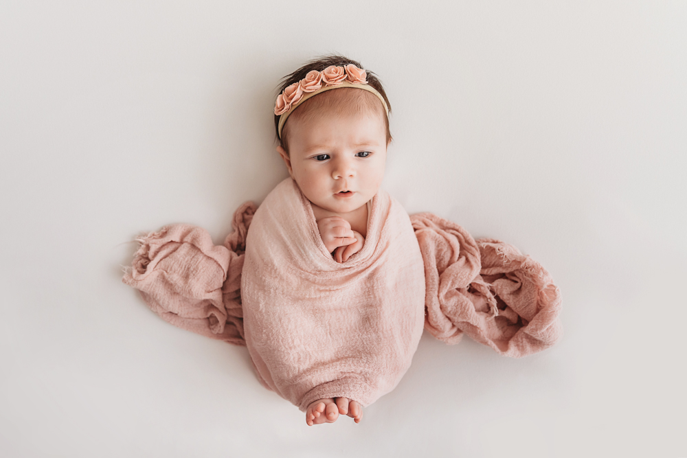 Awake portrait of Mary Katherine swaddled in a pink wrap with floral headband and textured layers at Reflection Images by Tracy Rowell in Florence SC
