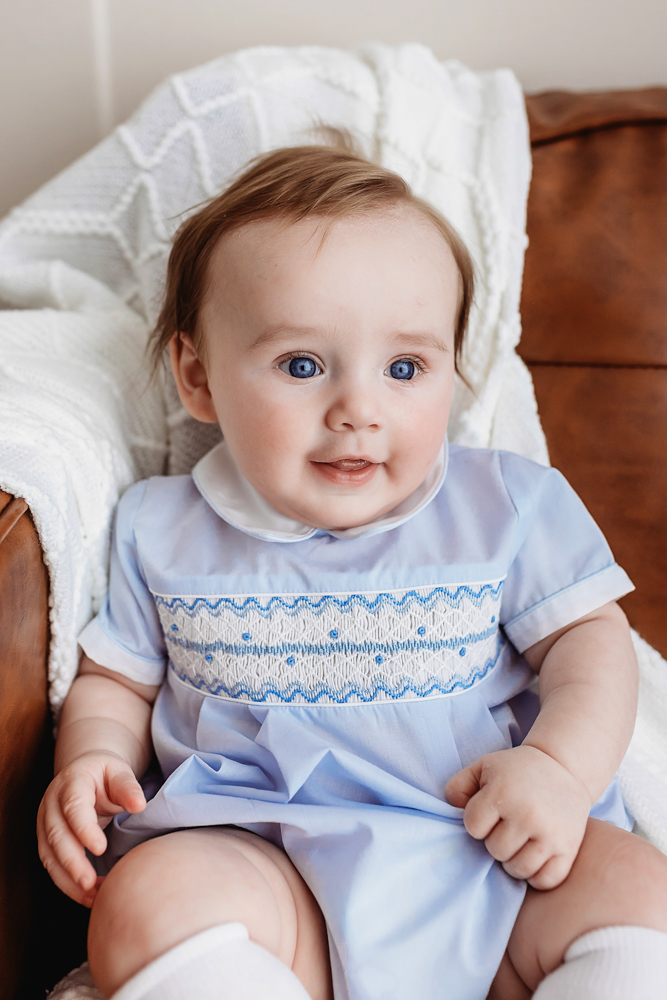 Smiling baby in blue outfit on leather couch, milestone session Reflection Images by Tracy Rowell