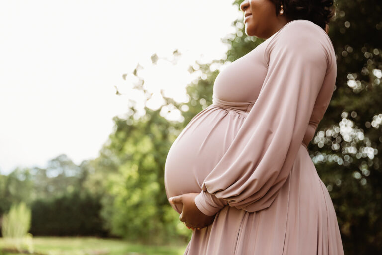 Profile close up of baby bump with flowing mauve sleeves and soft bokeh at Reflection Images in Florence SC.