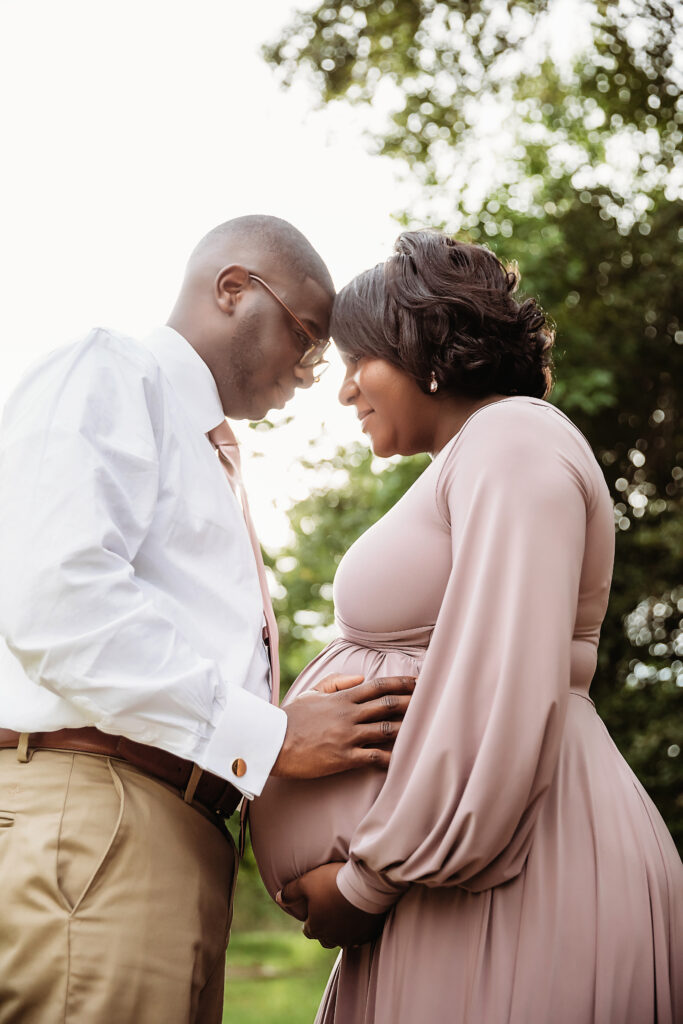 Couple forehead-to-forehead, fathers hand on baby bump, tender outdoor maternity moment at Reflection Images by Tracy Rowell in Florence SC.