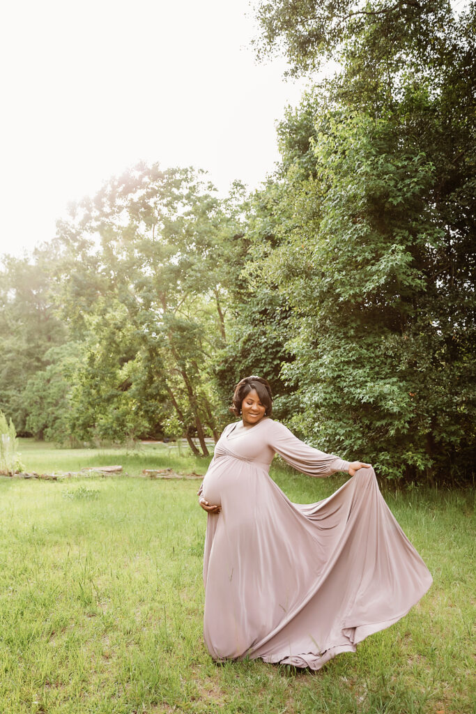 Mother-to-be in flowing lavender gown twirling gracefully in a sunlit field at Reflection Images by Tracy Rowell in Florence SC.