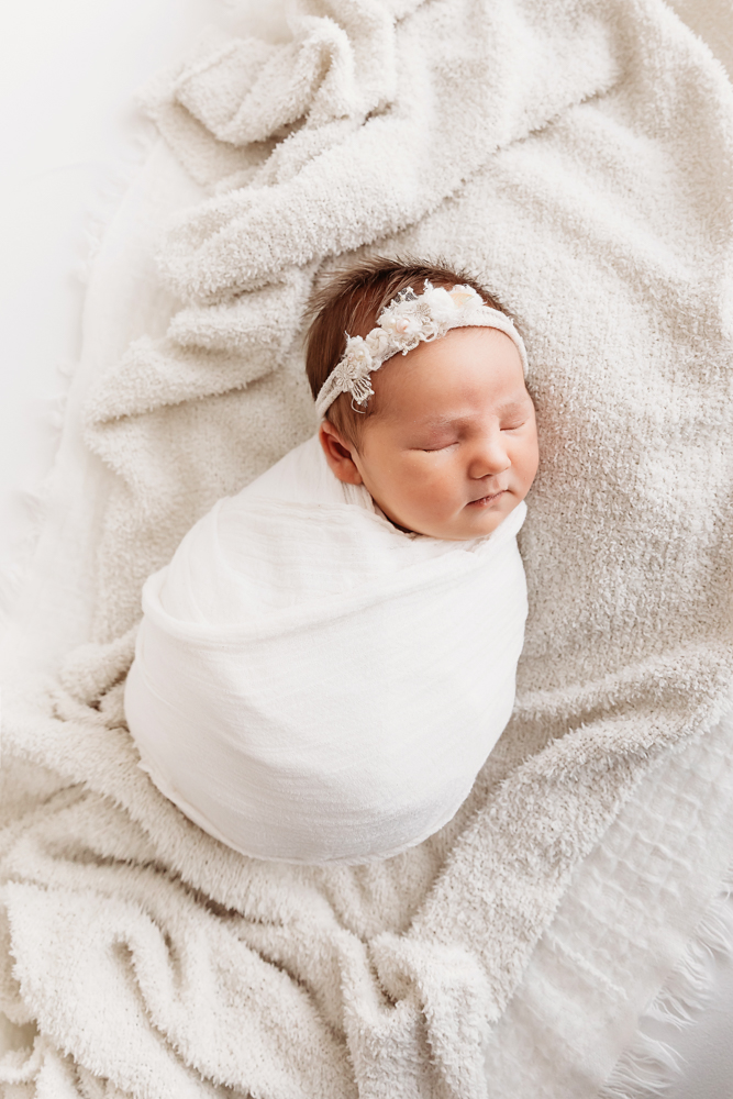 Newborn baby swaddled in white wrap, lying on textured cream blanket at Reflection Images by Tracy Rowell in Florence SC.