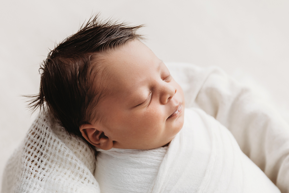 Side profile close-up of newborn Liston swaddled in white with textured blanket in a basket at Reflection Images by Tracy Rowell in Florence SC