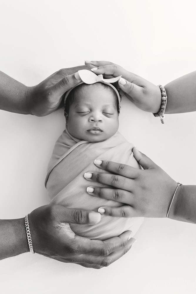 Newborn Harlem wrapped in purple with familys protective hands surrounding her, overhead studio view at Reflection Images by Tracy Rowell in Florence SC