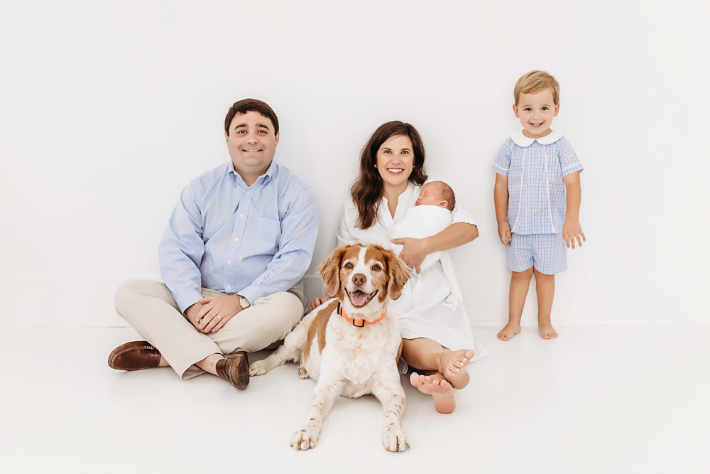 Family sitting on white floor with Darla the dog in front and baby Harry in moms arms at Reflection Images by Tracy Rowell in Florence SC