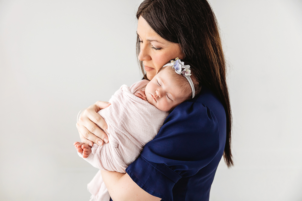 Mary Katherine sleeping peacefully on moms chest, swaddled in a soft blush wrap with lilac headband at Reflection Images by Tracy Rowell in Florence SC