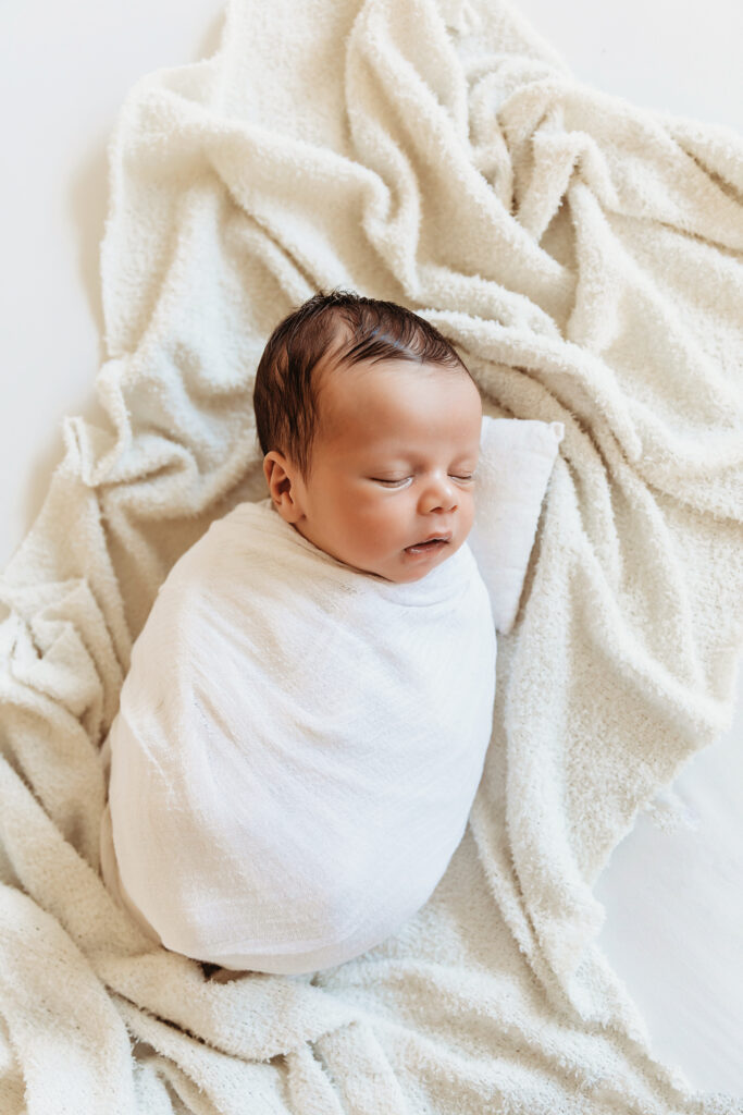 Newborn baby peacefully sleeping wrapped in white on a cozy white blanket at Reflection Images by Tracy Rowell in Florence SC