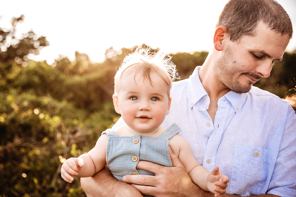 Close-up of baby Cole in a chambray romper held by dad with soft backlighting and greenery at Reflection Images by Tracy Rowell in Florence SC