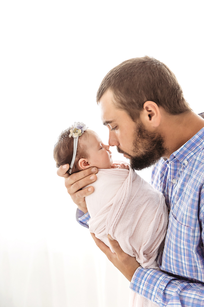 Dad holding Mary Katherine and kissing her nose in front of bright studio window at Reflection Images by Tracy Rowell in Florence SC