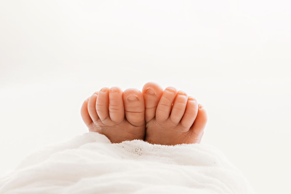Macro closeup of newborn toes peeking from white wrap at Reflection Images by Tracy Rowell in Florence SC.