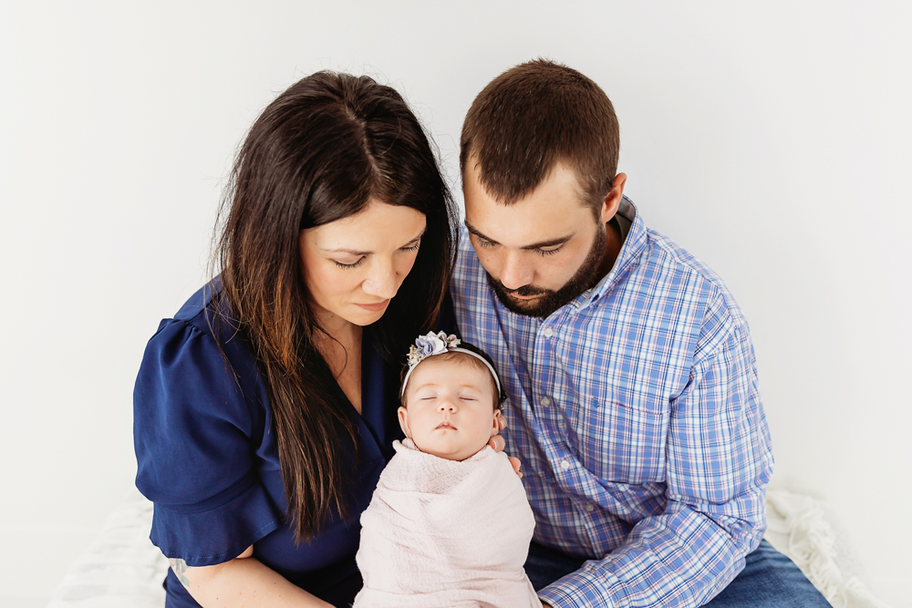 Mary Katherine swaddled in blush wrap held by mom and dad during a quiet moment at Reflection Images by Tracy Rowell in Florence SC