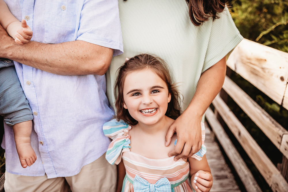 Stella grinning brightly with her moms arm around her on a sunlit boardwalk at Reflection Images by Tracy Rowell in Florence SC