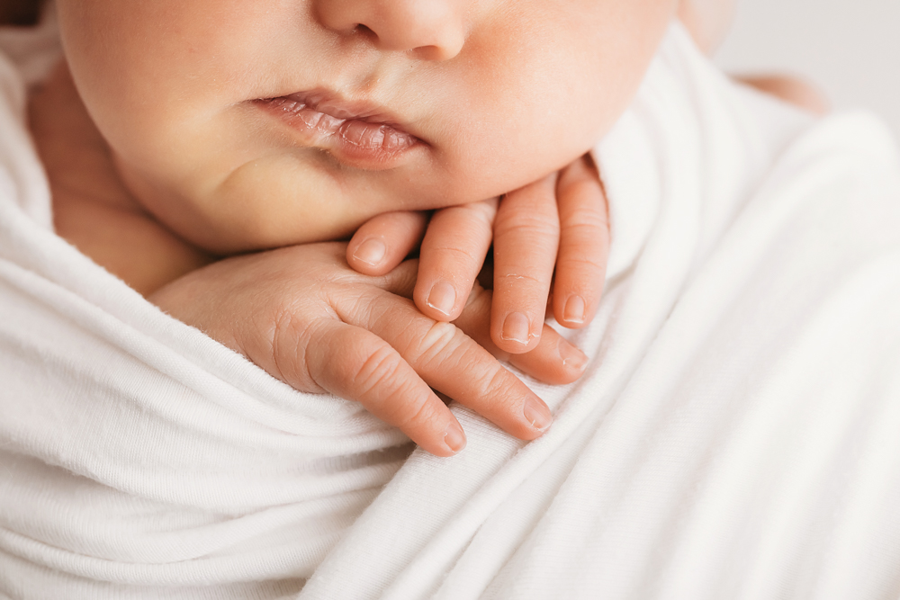 Close-up of baby resting chin on folded hands in white wrap at Reflection Images by Tracy Rowell in Florence SC.