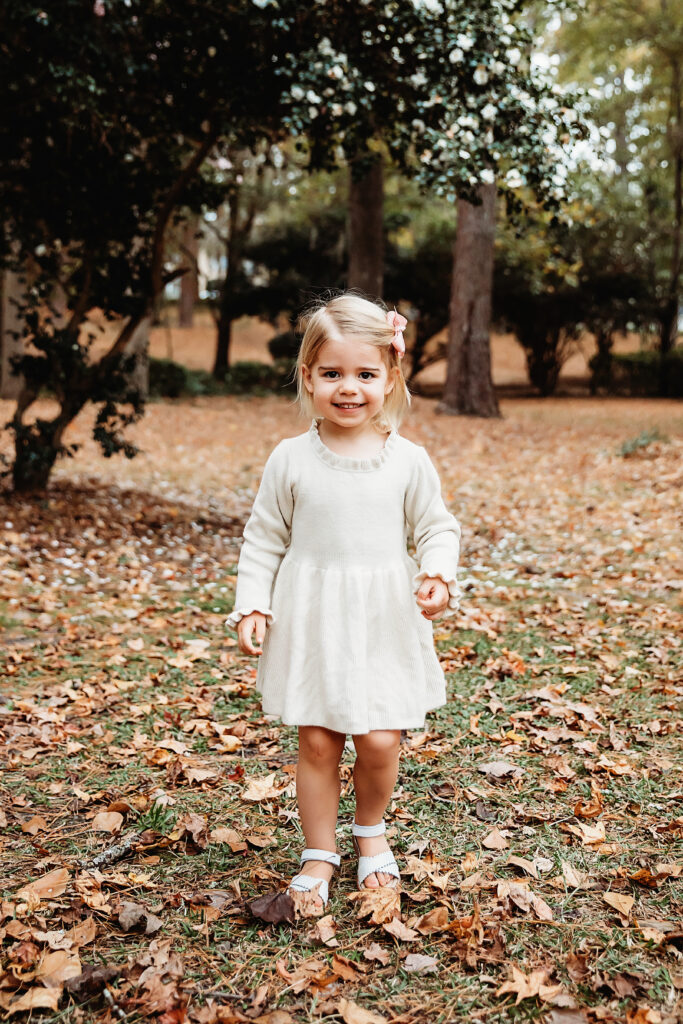 Toddler girl smiling in cream dress and pink bow during outdoor maternity session at Reflection Images by Tracy Rowell in Florence SC