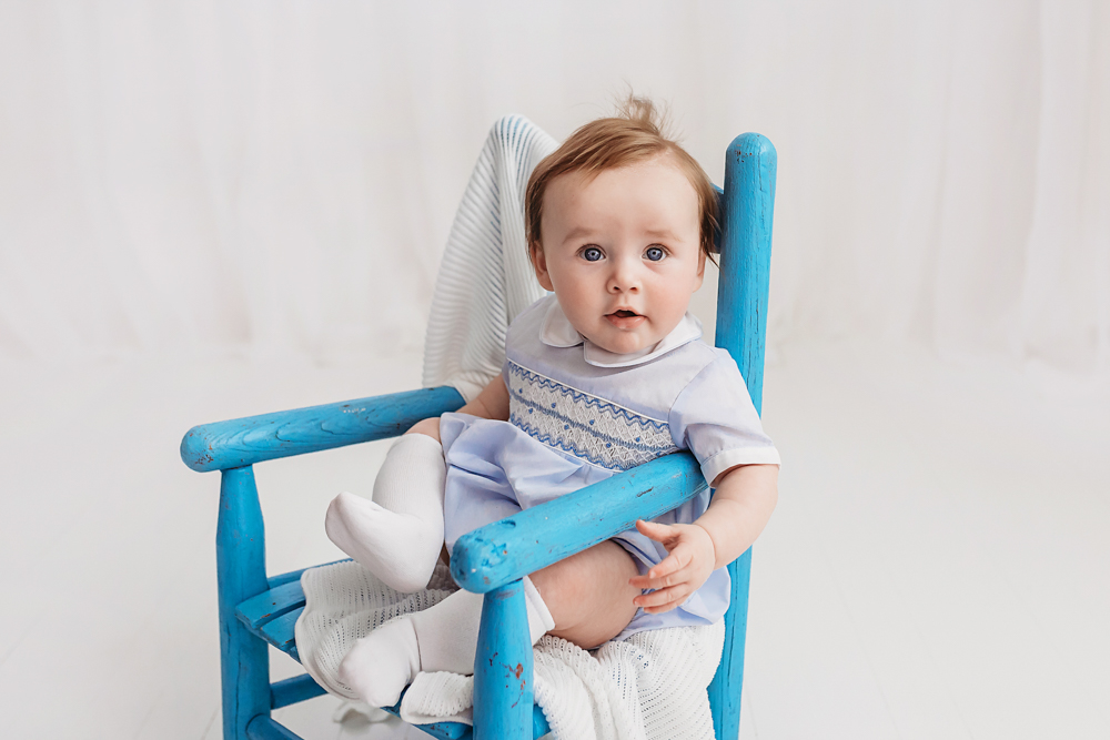 Baby boy smiling in blue chair with white blanket, professional milestone session Florence SC