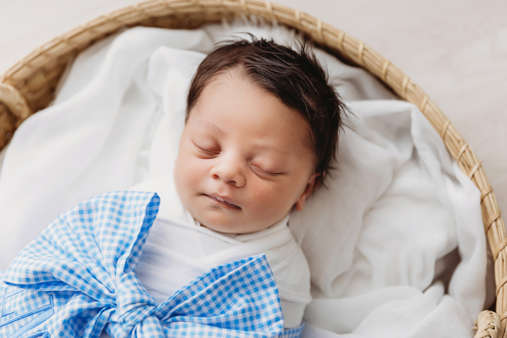 Tightly framed shot of newborn Liston with soft expression, swaddled in white and accented with a blue gingham bow in a basket at Reflection Images by Tracy Rowell in Florence SC