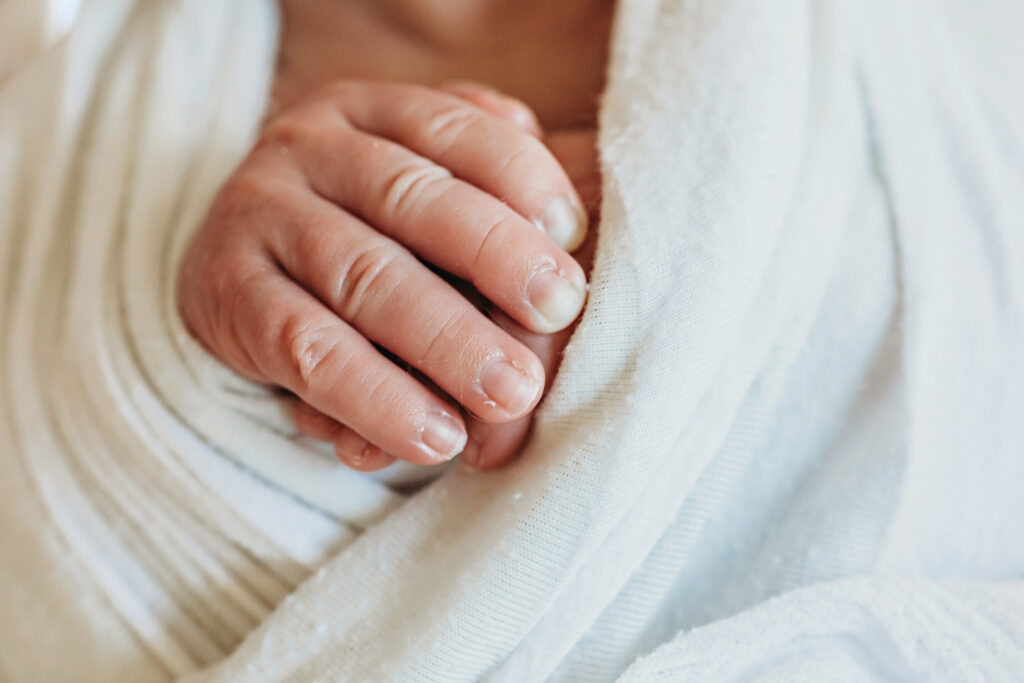 Newborns tiny fingers resting over white wrap, in a close-up composition at Reflection Images by Tracy Rowell in Florence SC