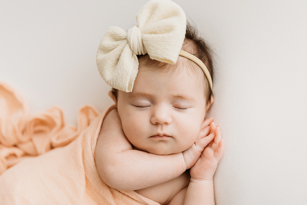 Mary Katherine wrapped in a soft peach fabric with matching bow, resting peacefully against a white backdrop at Reflection Images by Tracy Rowell in Florence SC