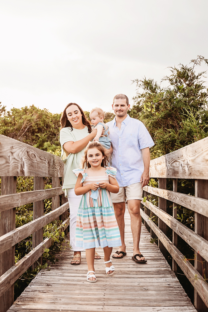 The Skinner family walking forward on a boardwalk with bright smiles and coastal greenery behind them at Reflection Images by Tracy Rowell in Florence SC