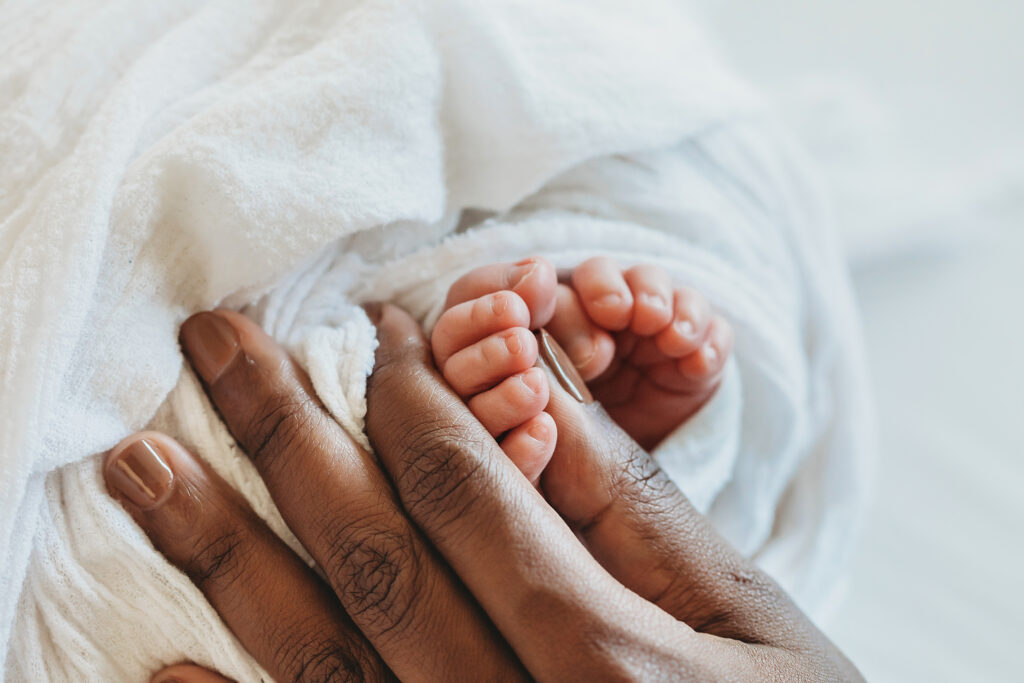 Tiny newborn toes held in mothers hand, wrapped in white blanket at Reflection Images by Tracy Rowell in Florence SC