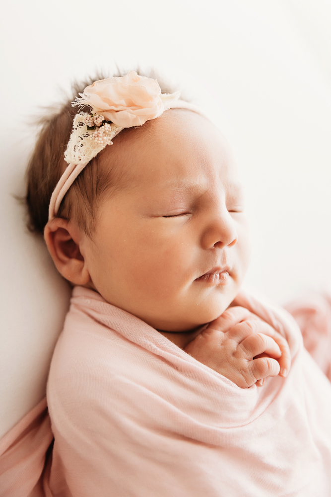 Closeup of newborn swaddled in blush pink wrap with delicate headband at Reflection Images by Tracy Rowell in Florence SC.
