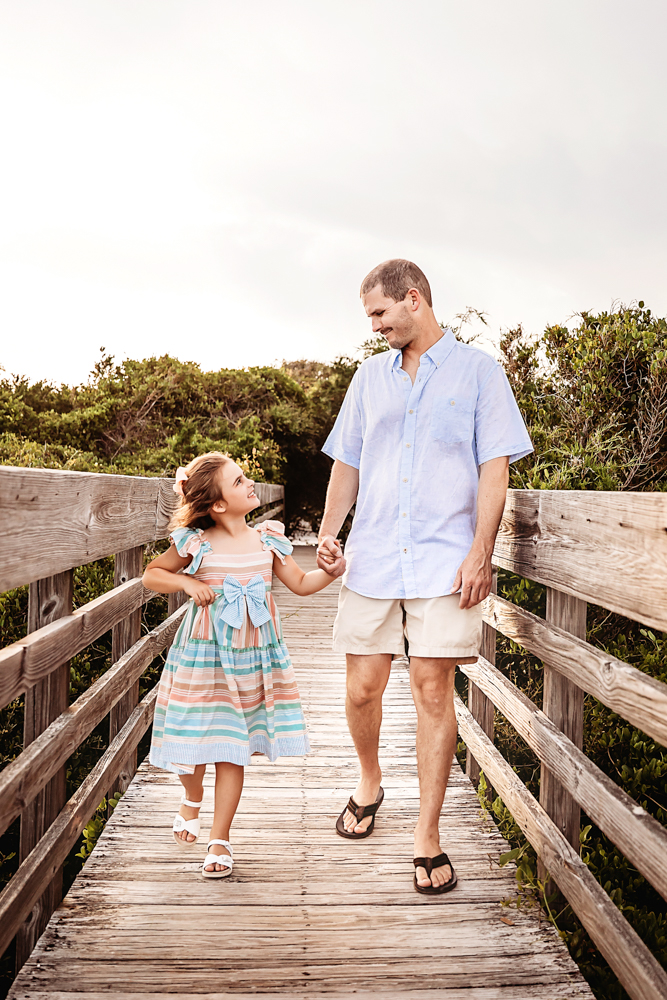 Stella and dad walking hand-in-hand on a beach boardwalk with loving smiles at Reflection Images by Tracy Rowell in Florence SC