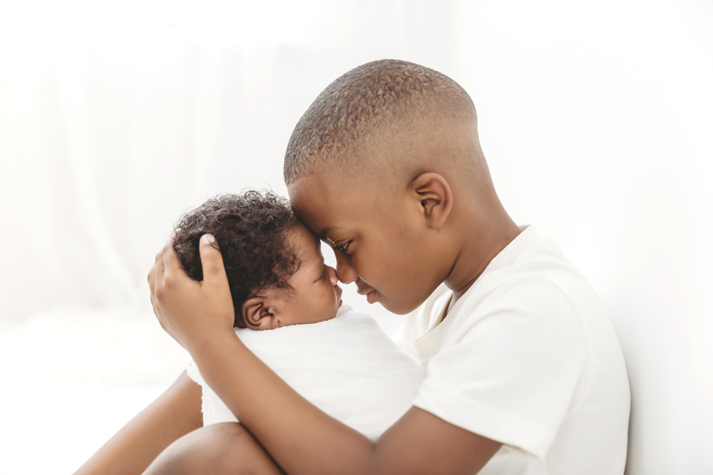Forehead-to-forehead moment between big brother and swaddled Braylen, soft white tones at Reflection Images by Tracy Rowell in Florence SC