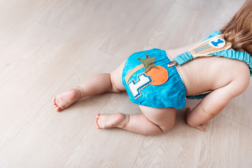 Close-up detail of Levi crawling in a turquoise birthday romper with a felt peach and number one patch during his session at Reflection Images by Tracy Rowell in Florence SC